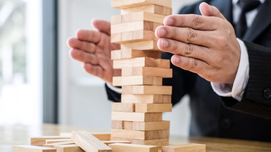 uomo con mattoncini di legno in equilibrio a simbolo della protezione dell'azienda